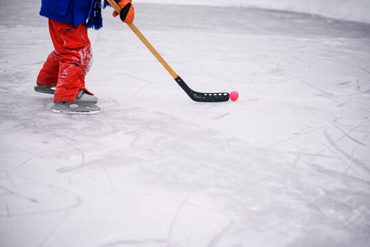 Close-up side view of a boy's legs in skiwear on a frozen pond playing ice hockey