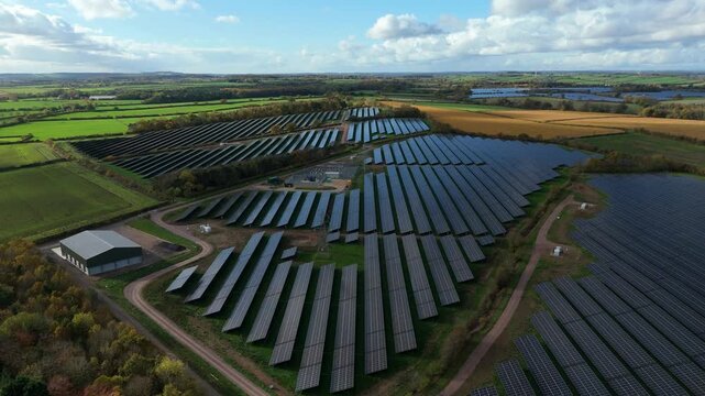 - Aerial drone over large solar power plant showing rows of photovoltaic panels glinting in sunlight near Nottingham United Kingdom
