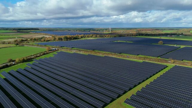 Drone flyover of utility solar field with maintenance tracks and inverter stations in a green landscape near Nottingham
