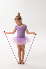 Young ballerina with cochlear implant looking at rope in her hands. Symbol of awareness, concentration, and childhood inclusion through art and technology.