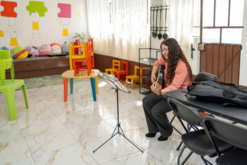 Smiling guitar teacher playing her instrument while reading sheet music, waiting in the classroom for her student to arrive. Concept of passion for teaching, music education, and creative expression