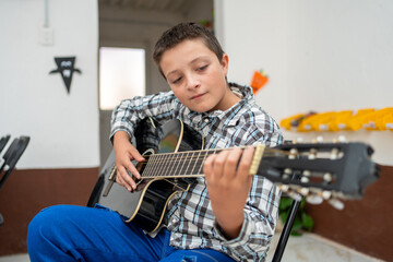 Portrait of a young boy playing acoustic guitar during his music lesson. Focused child musician learning instrument technique. Music education, talent, artistic growth