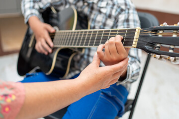 Close-up of teacher’s hand adjusting a young student’s hand on the acoustic guitar, showing correct playing position and technique. Music education, learning instrument, teaching guidance concept