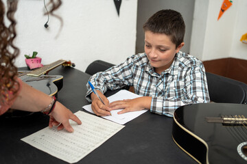 Guitar teacher helping a young student write and understand music notes during a private lesson. Focus on music theory, notation, and composition practice to improve reading and writing skills