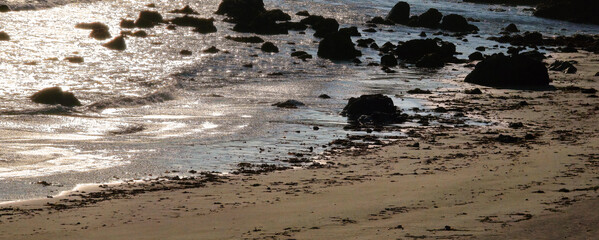 Dark photo of small waves rushing into black rocks and sandy beach after sunset w/Silvery...