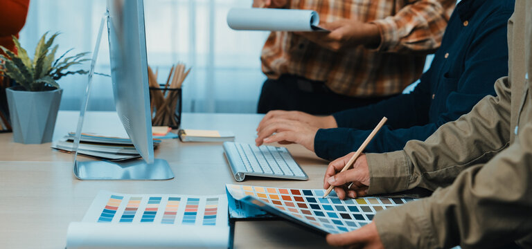 A diverse team works together in a modern office environment, selecting color palettes and designs while sharing ideas and resources for their creative project. SACTR - Powered by Adobe