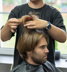 Fototapeta premium A hairdresser uses a pair of scissors to cut a male client's long blonde hair.