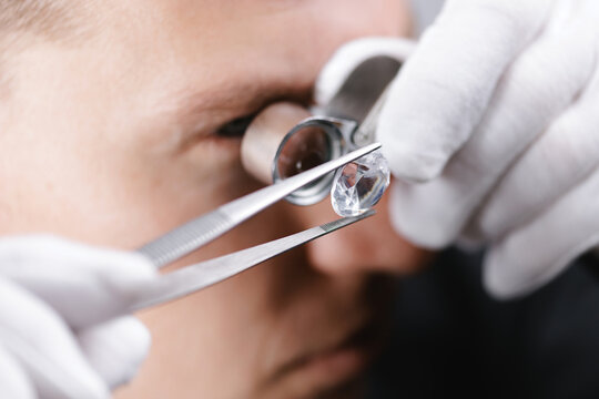 Caucasian male jeweler examining diamond with magnifying glass and tweezers, closeup process