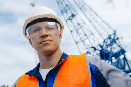 Male worker at shipyard with crane in background: safety, construction, and cargo industry focus