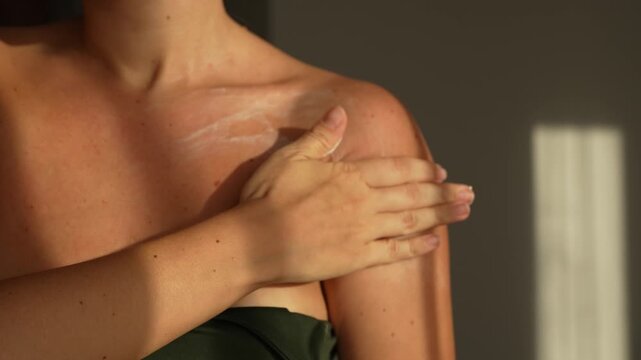 Young woman applying moisturising cream on chest and shoulder in warm sunlight, skincare and self love morning ritual