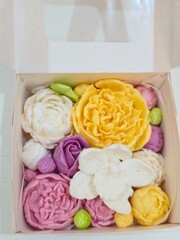 Close-up of a box filled with decorative flower-shaped marshmallows or  zephyr in various colors: white, yellow, pink, and purple