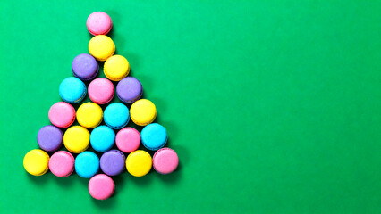 Obraz premium Christmas tree made of bright colorful macaroons on a green background, space for text