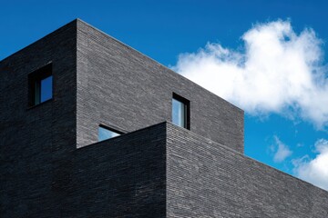 Modern architectural design featuring dark brick and sharp angles against a blue sky with clouds, showcasing innovative urban construction techniques