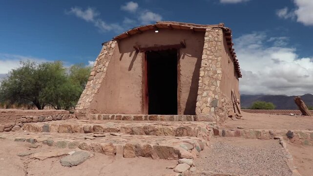 Restored adobe chapel in Anillaco, Catamarca, Argentina. Close-up view of the historic architecture with stone base against mountains.