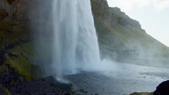 A powerful cascade of water flows down the rocky cliffs of Seljalandsfoss, one of Iceland's most famous waterfalls. The footage captures the immense scale of the waterfall and the lush, green landscap