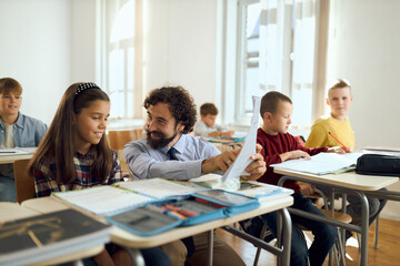 Mid adult male teacher assisting his student on a class at elementary school. 