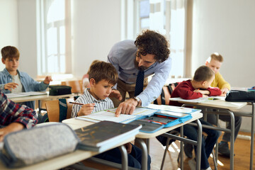 Happy male professor talking to schoolboy while assisting him on a class at elementary school.