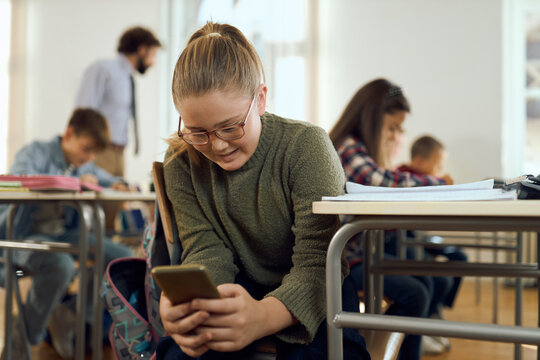Smiling elementary student using mobile phone while having a class with her friends at elementary school - Powered by Adobe