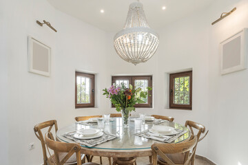 Dining set with a round natural teak table and Balinese-style chairs, with a tropical bouquet of heliconias and birds of paradise.