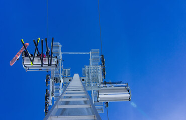 Fototapeta premium Low-angle perspective, looking straight up at a modern, high-speed chairlift system against an intense, clear blue sky