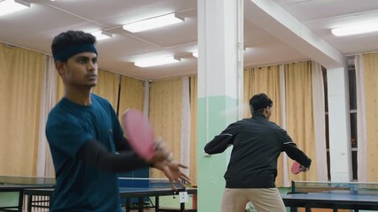 Two athletes engaged in table tennis practice indoors, one player preparing to return shot while opponent stands ready across table, showcasing intensity and movement during competitive training - Powered by Adobe