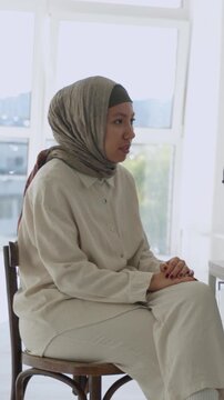 Vertical video young islamic woman wearing a hijab sitting on a chair and talking during a psychology consultation or a group therapy session, sharing her problems and receiving support