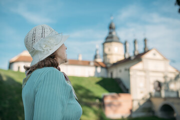 Пожилая довольная женщина гуляет на экскурсии в парке возле старинного замка. Пенсионерка рассматривает историческую архитектуру.
