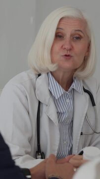Vertical video experienced woman physician using a stethoscope to discuss medication and providing a patient with a pill bottle in her contemporary, well-lit office within the hospital