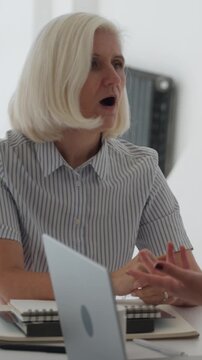 Vertical video senior female doctor with gray hair leading a discussion on patient cases and treatment strategies with her diverse team of colleagues at a medical seminar in a modern hospital setting