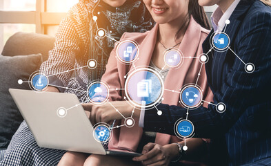 Three professionals collaborate over a laptop, engaging with digital icons that symbolize networking and teamwork, creating an innovative office atmosphere. Tessel