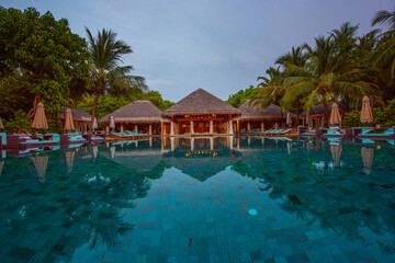 Tranquil closeup calm sea water waves with palm trees. Cabins with pool. Tropical island beach landscape exotic shore coast. Summer vacation, holiday amazing nature. Relax paradise, Maldives.