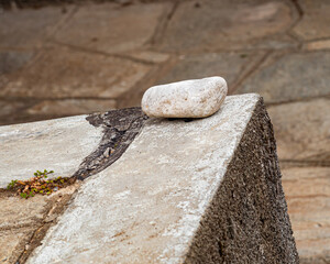 Close-up of a smooth white stone placed on a textured concrete surface outdoors. The minimal composition evokes calm, balance, and contrast between nature and construction materials