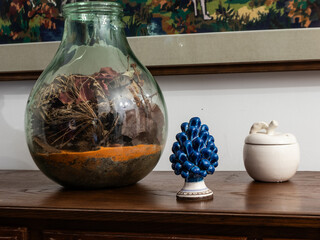 Close-up of decorative objects on a wooden cabinet: a glass vase with dried plants, a blue ceramic pine, and a white ceramic container. Perfect for home decor and craftsmanship themes