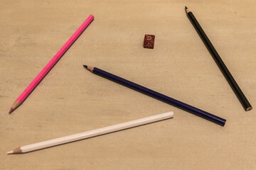 Colored pencils and a red polyhedral die arranged on a beige desk. Perfect for creativity, education, design, or tabletop gaming concepts