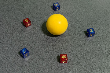 Yellow ball surrounded by colorful dice on a gray surface, symbolizing balance, creativity, randomness, and game strategy in a minimalist composition