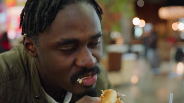 Close up of man biting burger with satisfactory smile, blurred bokeh lights in background, casual dining atmosphere highlighting lifestyle, food enjoyment, and everyday eating