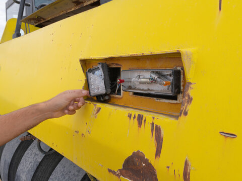 hispanic Worker's hand checking a broken led work light on a yellow heavy machinery vehicle, indicating maintenance or repair