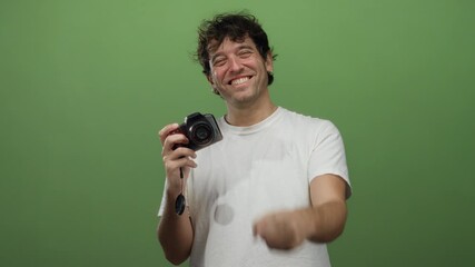 Hispanic man holding camera pointing with a smile against green background, capturing the essence of joyful photography.