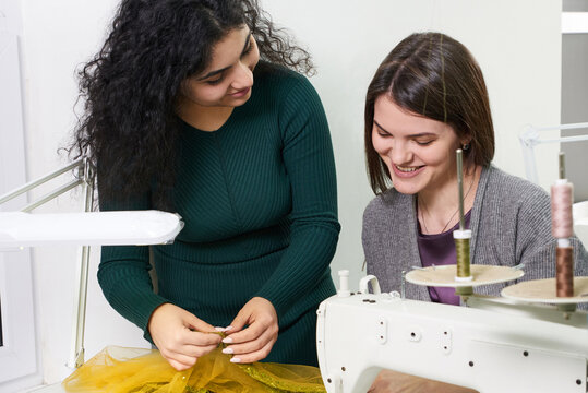 Pretty seamstress teaching girl working with sewing machine at sewing class in tailor studio