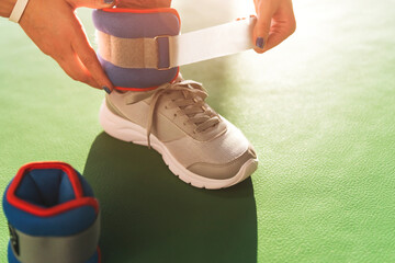 Woman putting on ankle wights before she starts a workout in a gym, health and fitness concept