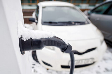 Frozen EV charging point with plug and wire covered in snow, eco-friendly transportation technology in cold season conditions. Snow covered charging connector for electric car close-up