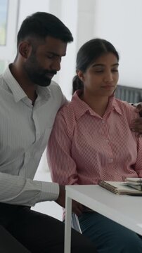 Vertical video loving indian husband supports and consoles distressed wife during a tense medical consultation, showing care and empathy