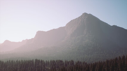 In this serene scene, the sun rises over a majestic mountain, casting a gentle glow over the rugged peak. Tall trees surround the base, creating a peaceful atmosphere in natures embrace.