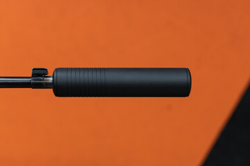 Fototapeta premium Close-up macro shot of a black firearm suppressor, or silencer, attached to a rifle barrel against a bright orange background.