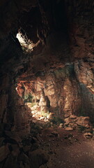 Inside a quiet cave, soft sunlight filters through the opening, casting gentle light on the rugged rocks. The scene reveals a serene atmosphere, untouched by human hands.