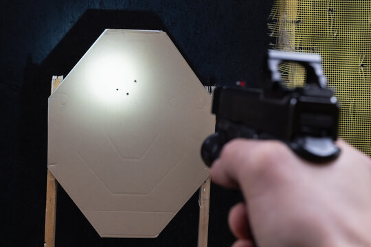 First-person view of aiming a tactical pistol with red dot sight and flashlight at a cardboard shooting target.