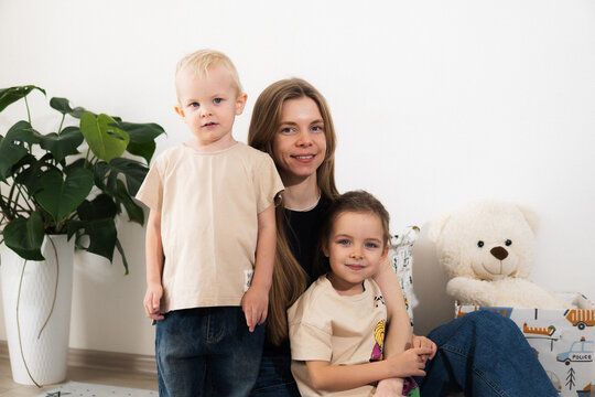 A happy mother with children at home is family happiness and care. A warm family scene of a blonde haired girl and two children sitting on the floor in a cozy room