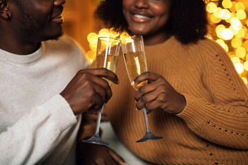 A young black couple joyfully makes a toast with champagne glasses. They celebrate Christmas in a cozy, decorated room filled with lights and festive spirit.