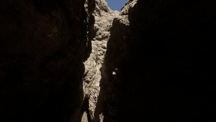 A narrow canyon reveals its rocky walls, bathed in sunlight and deep shadows. The bright blue sky peeks above, showcasing the beauty of natures unique formations and textures.