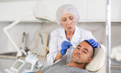Obraz premium Using Cold Hammer whitening of professional facial machine,woman beautician performs operation on man.